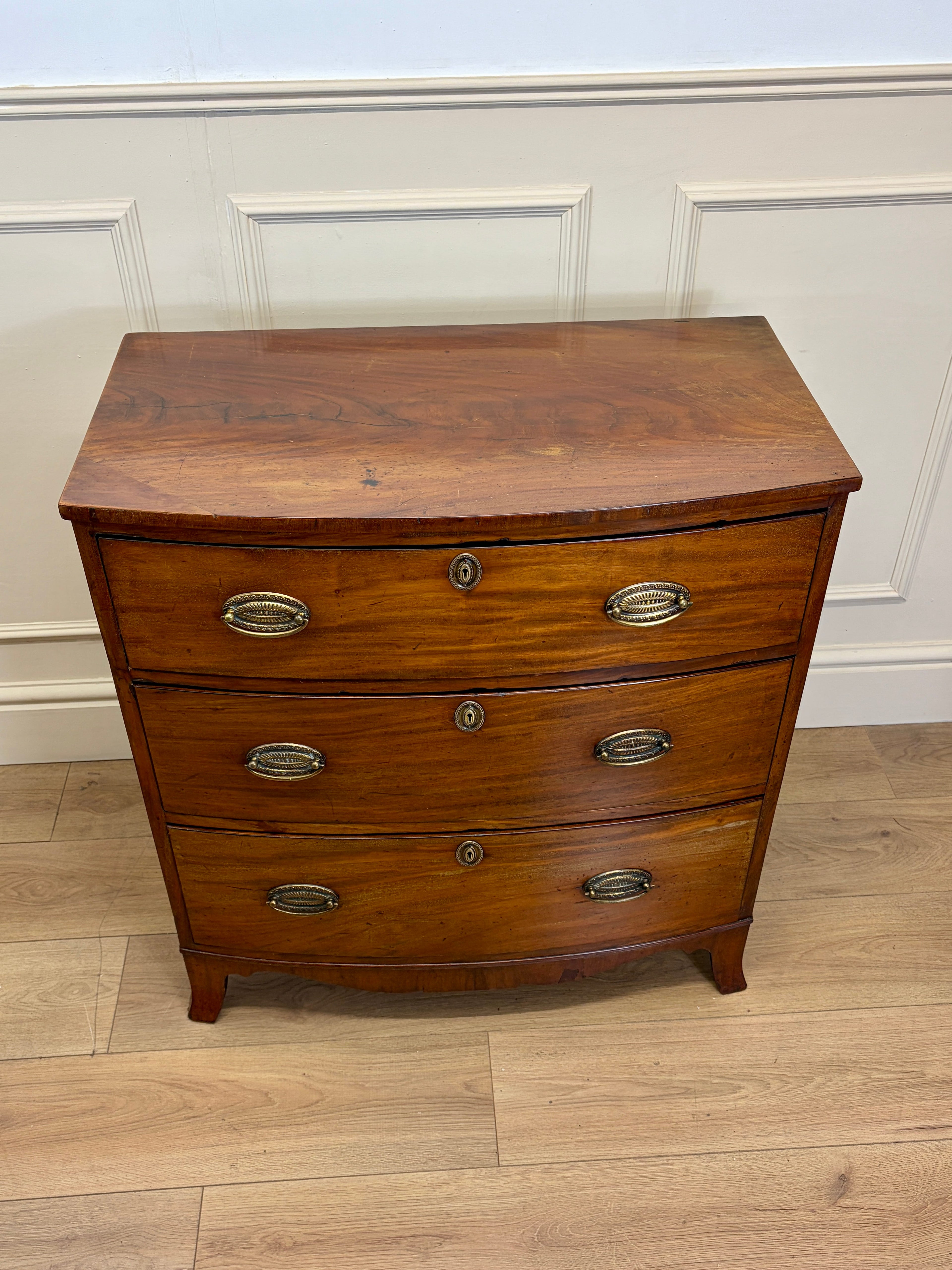 Wooden dresser with three drawers on a wooden floor against a white paneled wall.