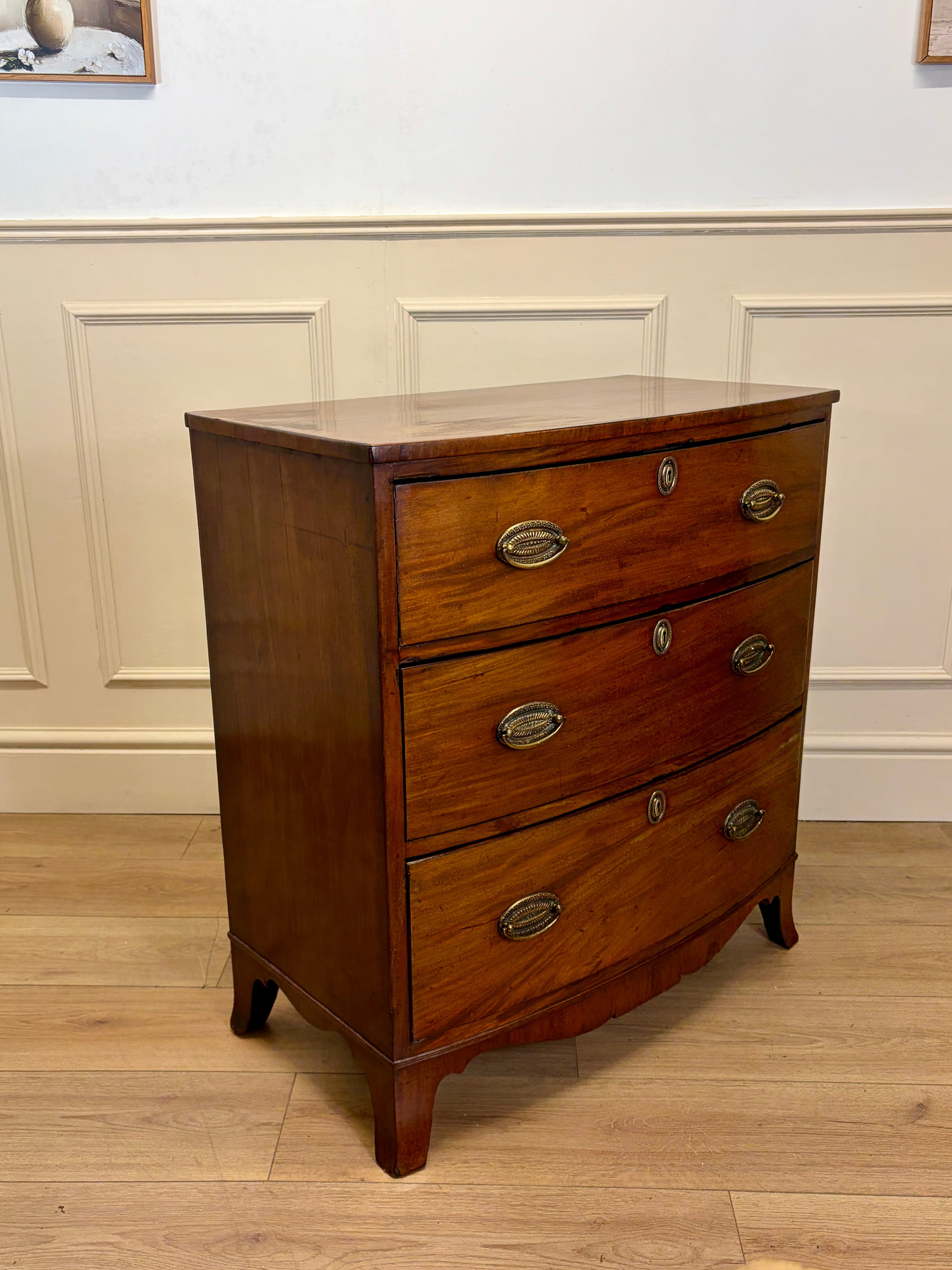Wooden dresser with three drawers against a white paneled wall.