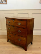 Wooden dresser with three drawers on a wooden floor against a white wall.