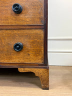 Close-up of a wooden dresser with two drawers and black knobs on a light wood floor.