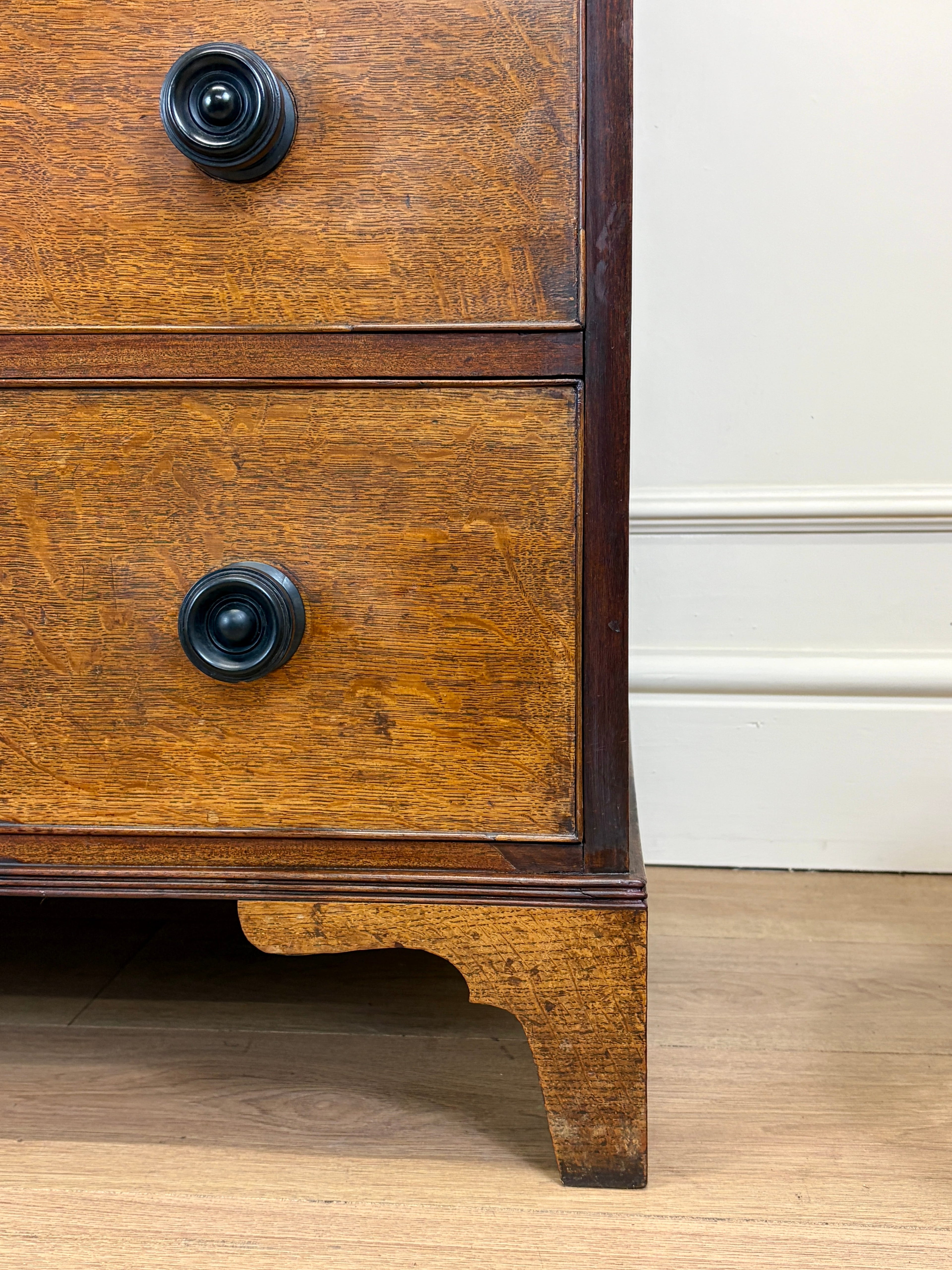 Close-up of a wooden dresser with two drawers and black knobs on a light wood floor.