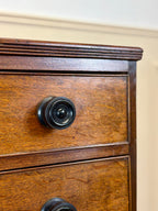 Close-up of a wooden drawer with black metal knobs on a beige wall background