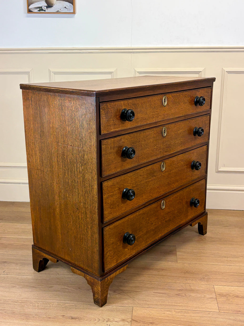 Wooden dresser with four drawers on a wooden floor against a white wall.