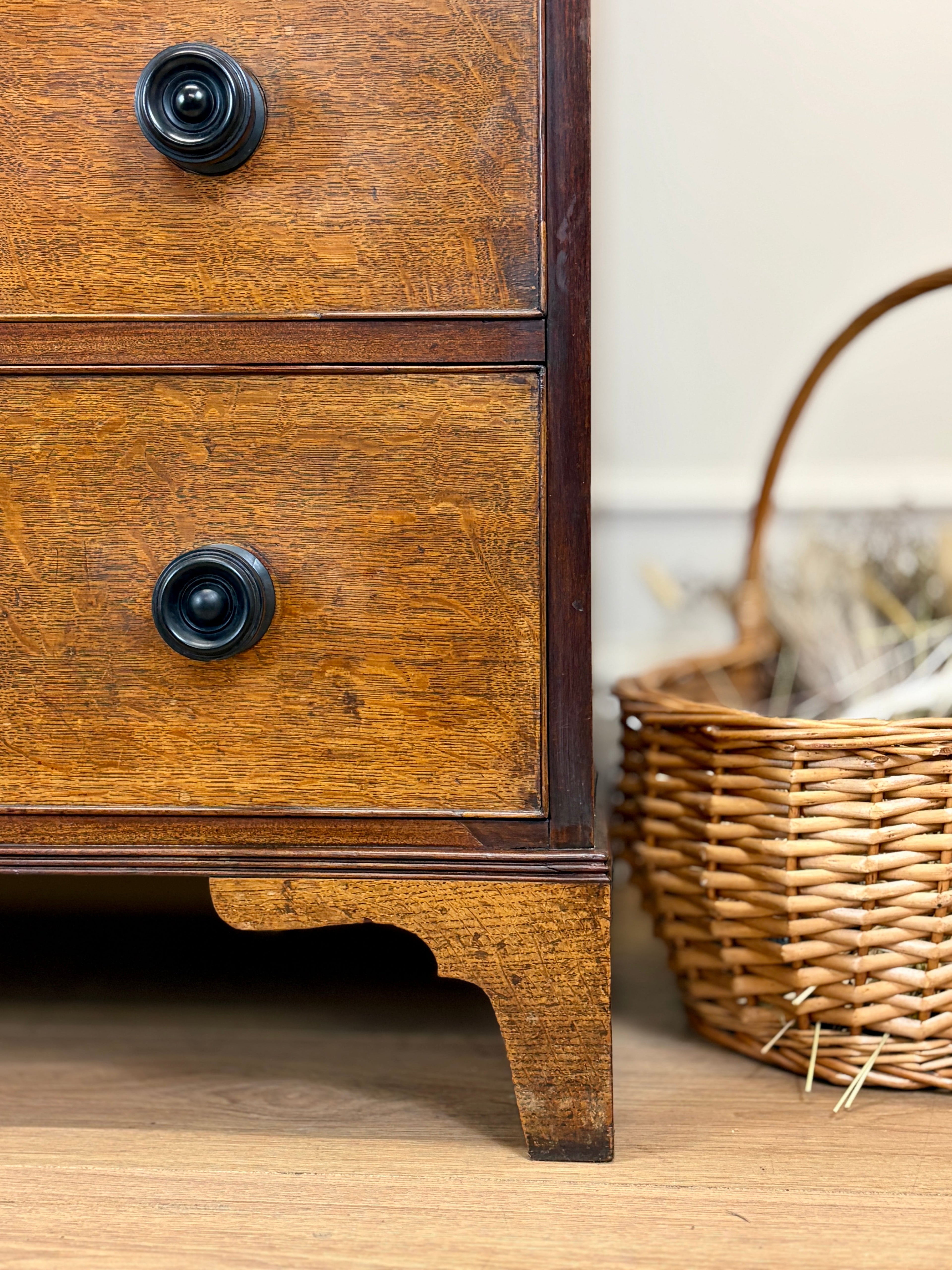 Wooden dresser with black knobs and a wicker basket on a wooden floor.