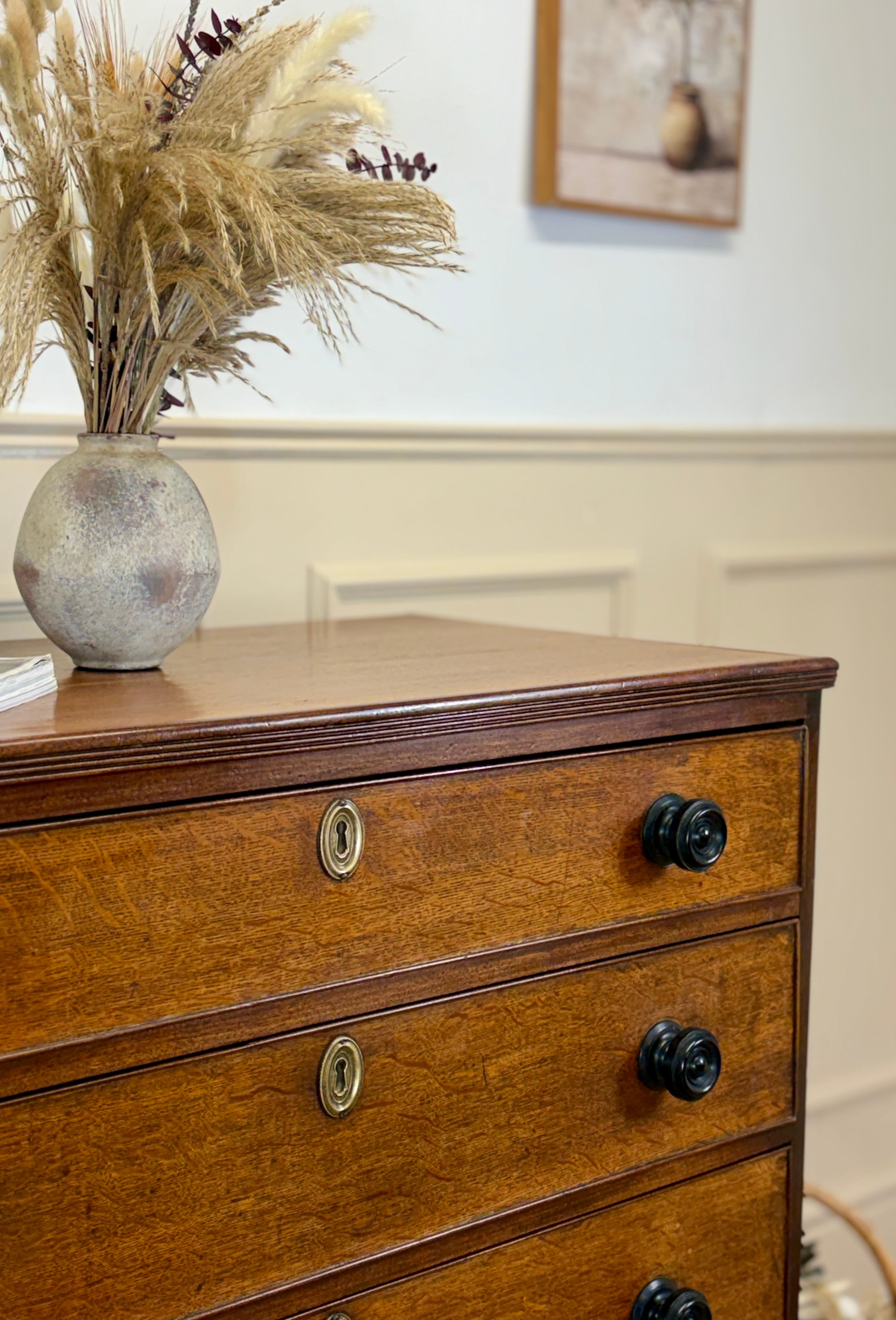 Wooden dresser with three drawers, each featuring a metal handle, against a neutral wall.