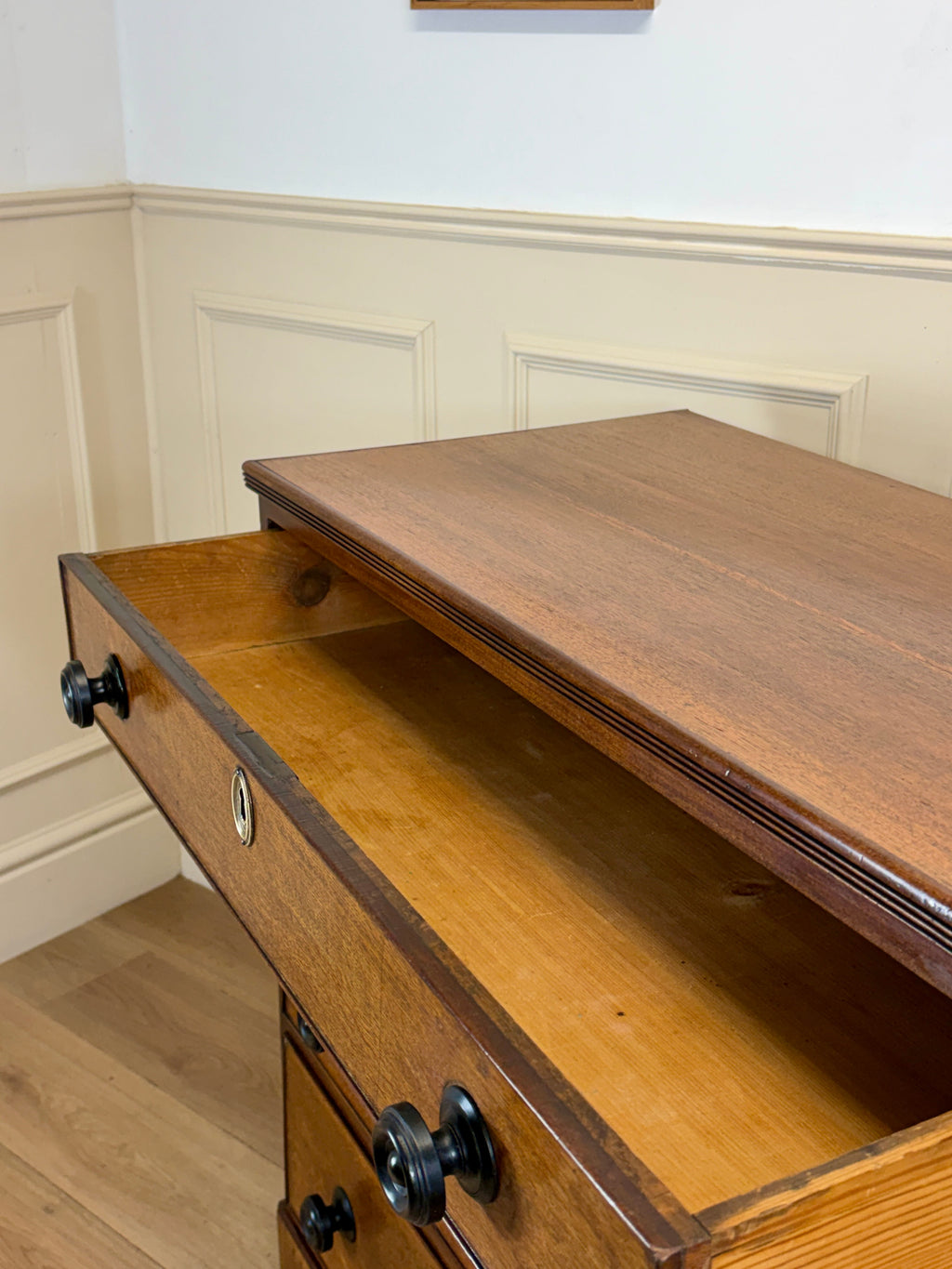 Wooden dresser with open drawer in a room with white walls and wooden floor.