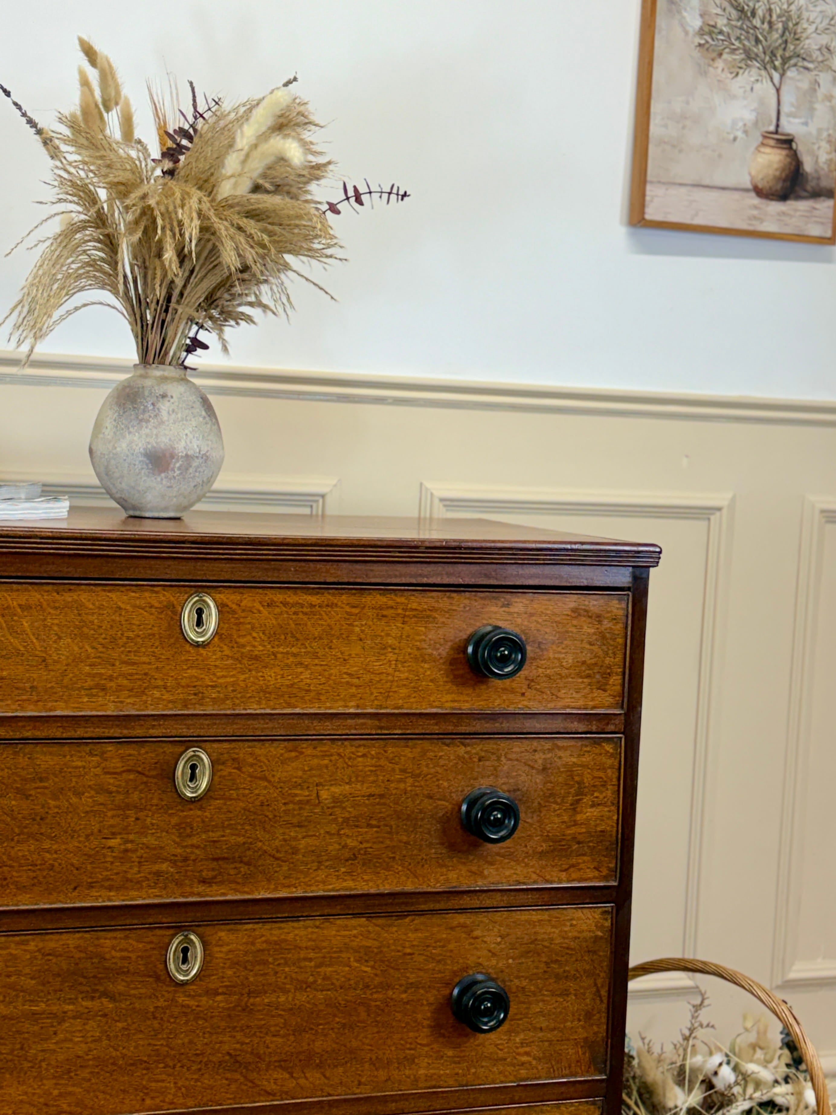 Wooden dresser with decorative items including a vase with pampas grass and a framed picture on the wall.