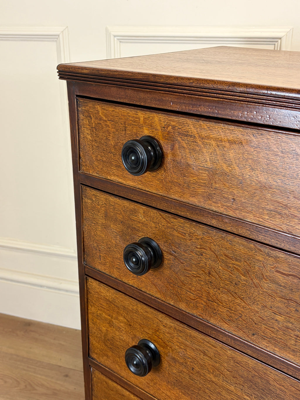 Wooden dresser with black knobs against a white wall.