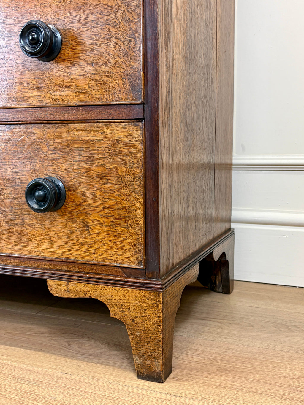 Wooden dresser with two drawers and black knobs on a wooden floor.