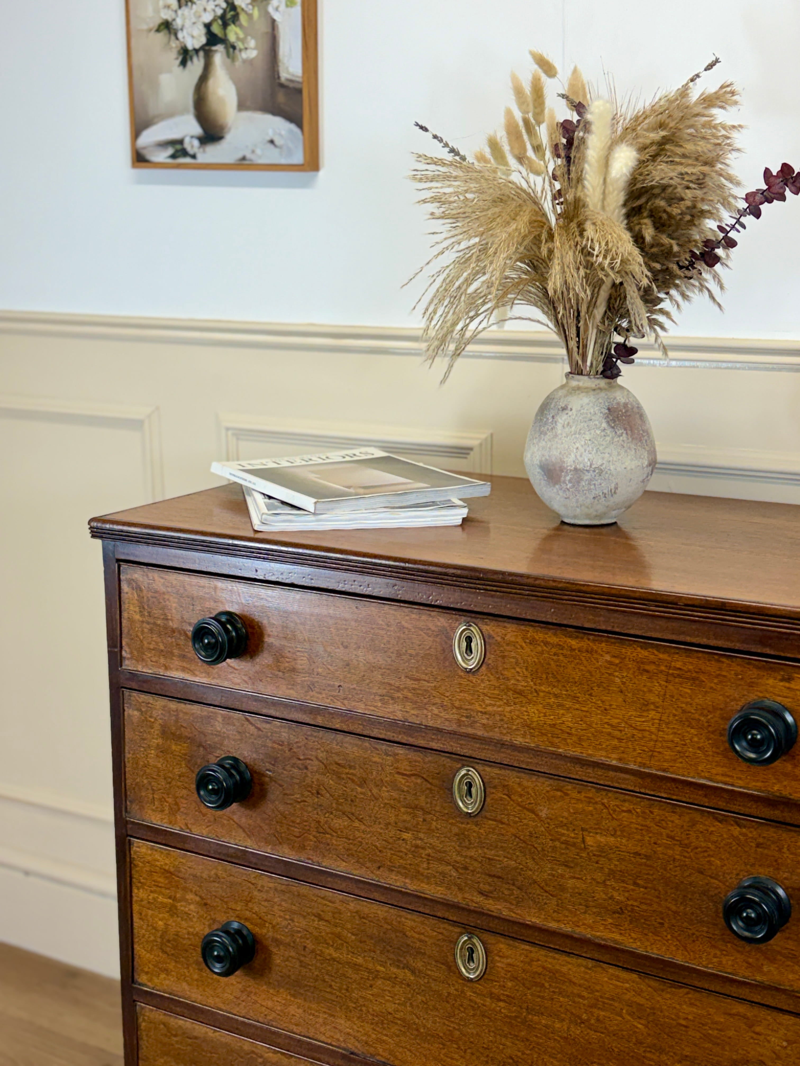 Wooden dresser with decorative items including a vase with dried plants and books.