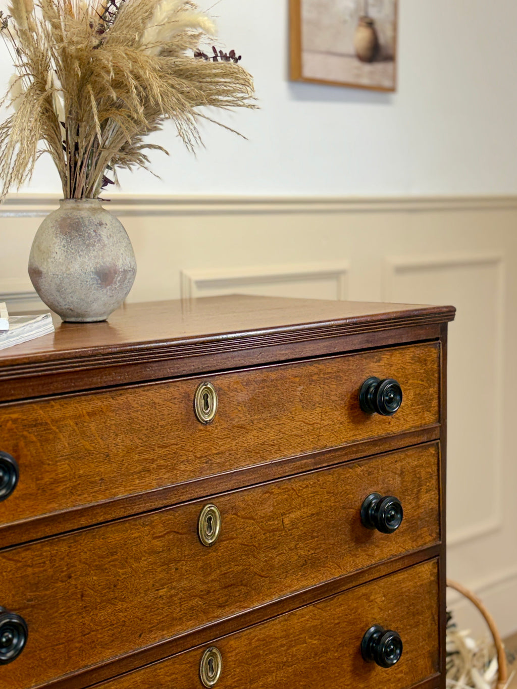 Wooden dresser with black knobs and a vase of pampas grass on top.