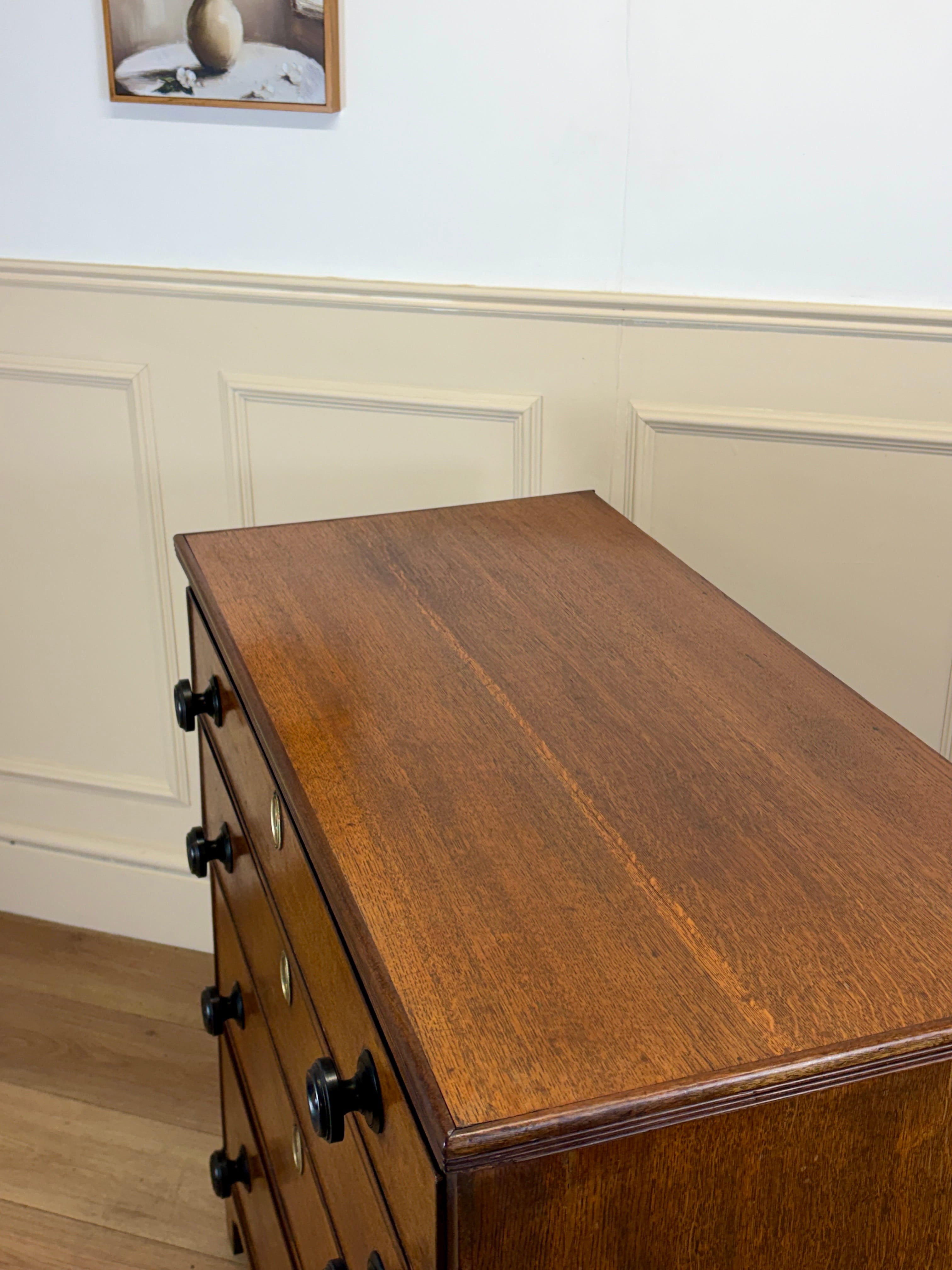 Wooden dresser with black handles against a white paneled wall.