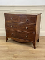 Wooden dresser with four drawers on a wooden floor against a white wall.