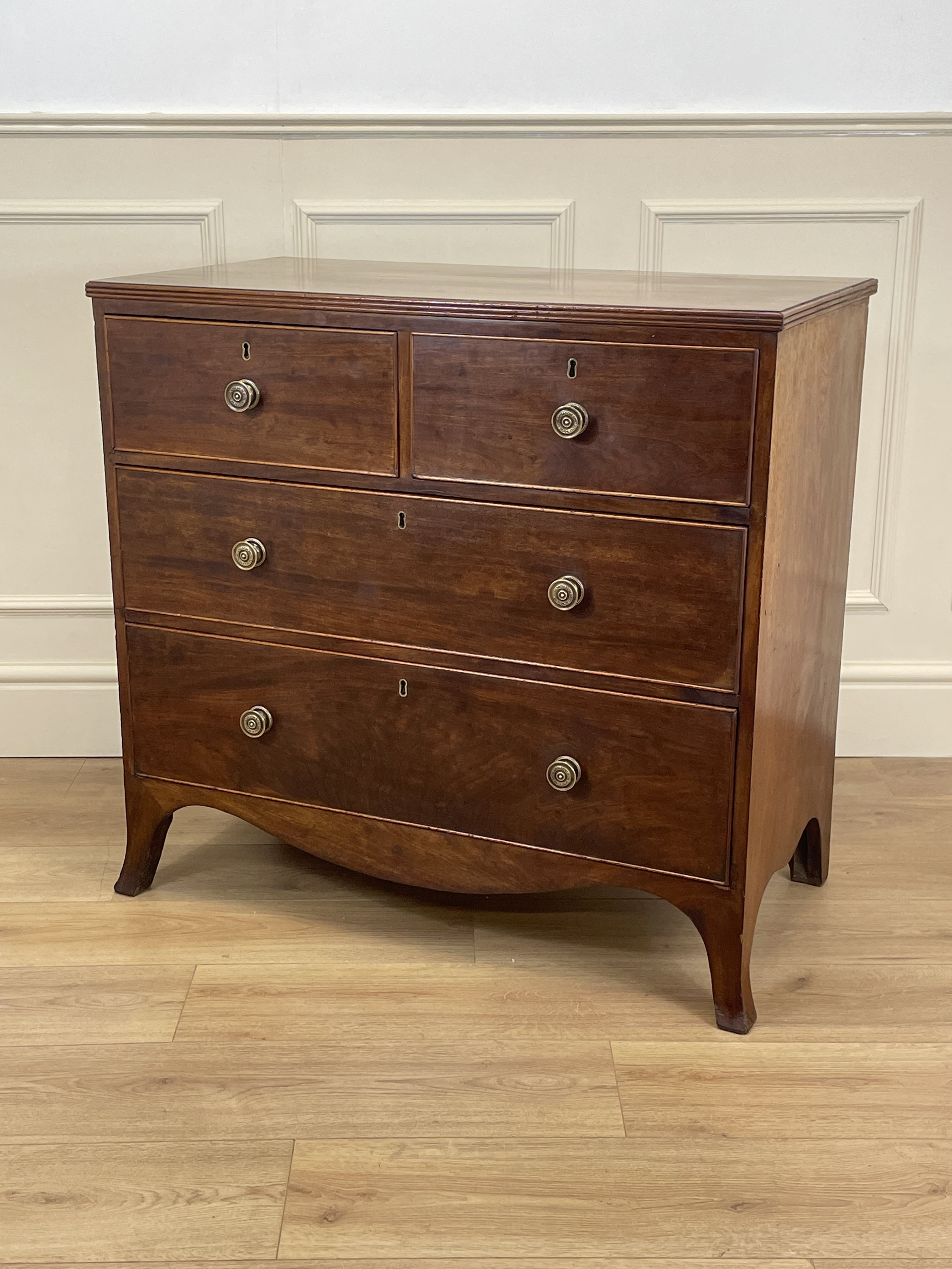 Wooden dresser with four drawers on a wooden floor against a white wall.