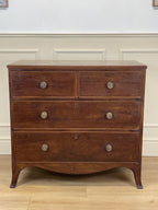 Wooden dresser with four drawers on a wooden floor against a white wall.