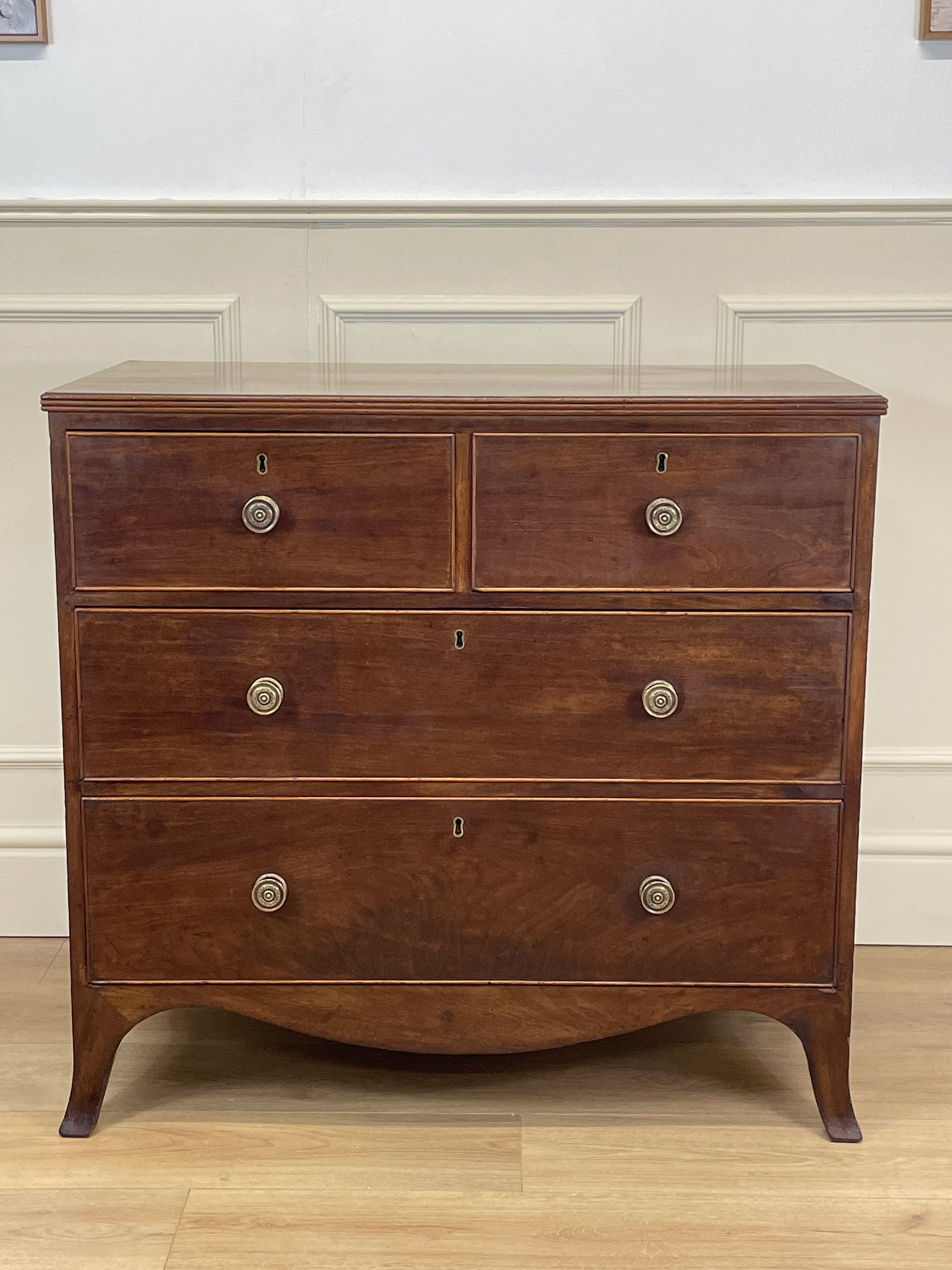 Wooden dresser with four drawers on a wooden floor against a white wall.