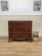 Wooden dresser with four drawers in a room with wainscoting and framed pictures.