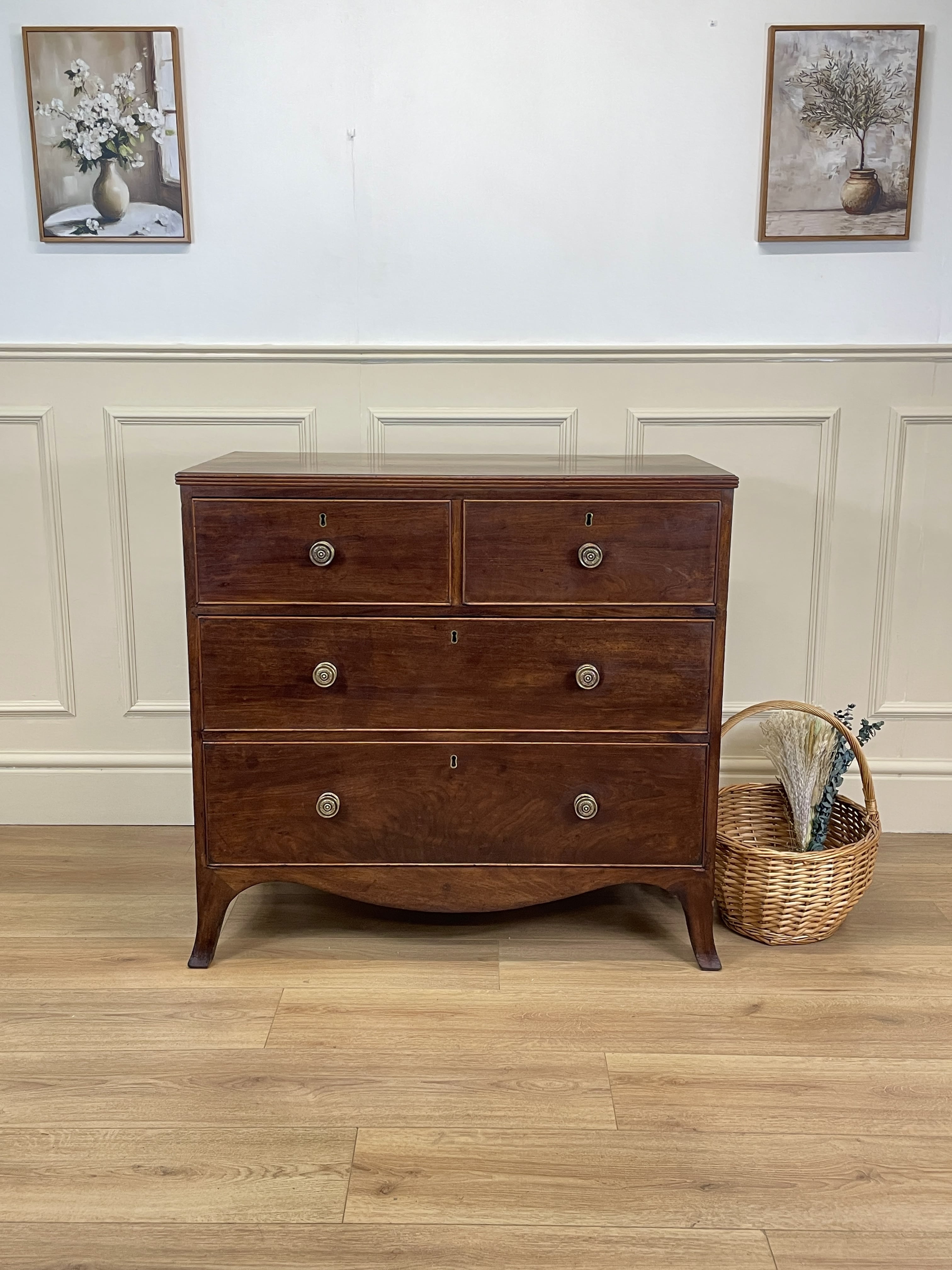 Wooden dresser with four drawers in a room with wainscoting and framed pictures.