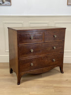 Wooden dresser with four drawers on a wooden floor against a white wall.