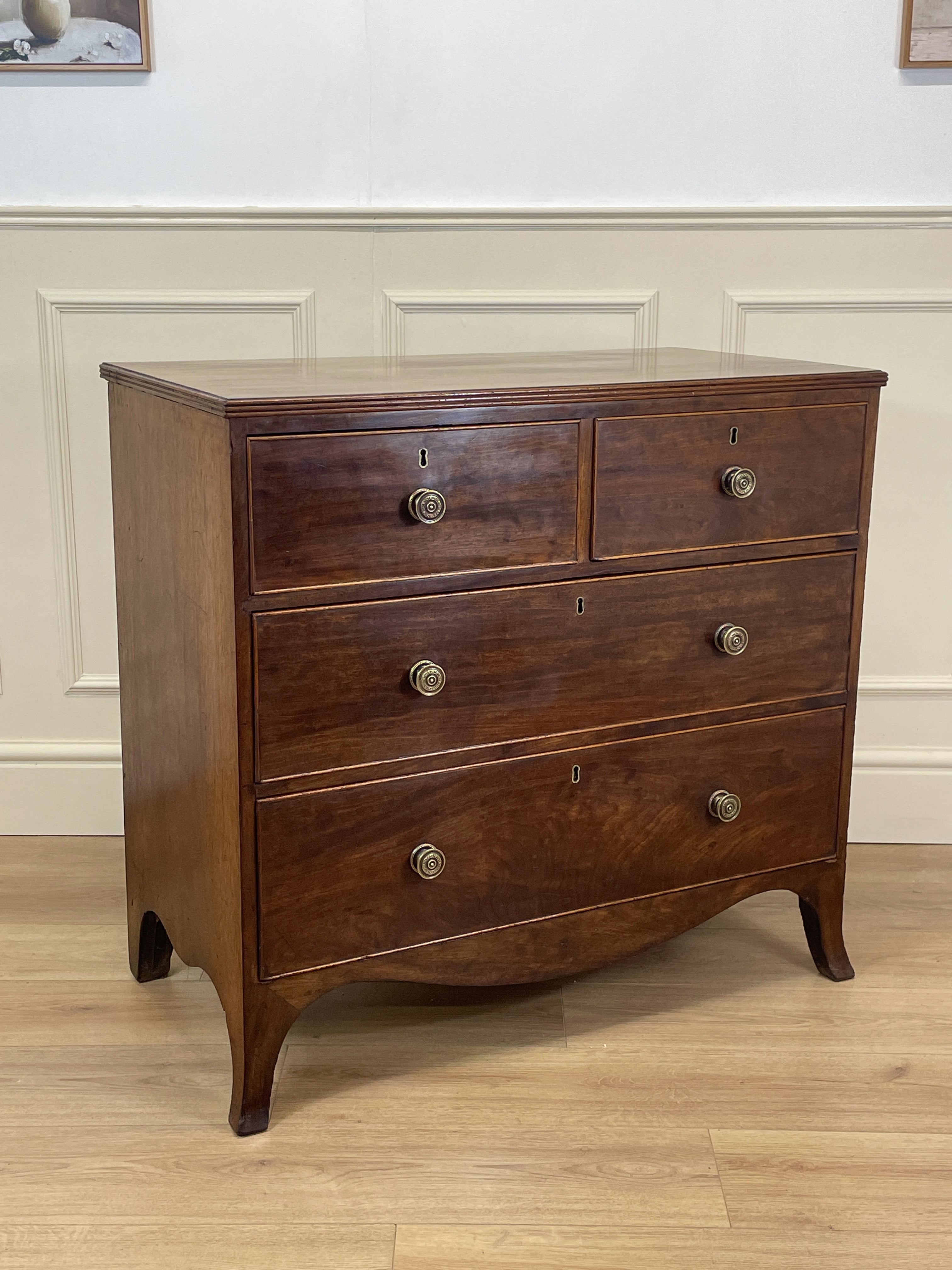 Wooden dresser with four drawers on a wooden floor against a white wall.