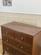 Wooden dresser with three drawers against a white paneled wall.
