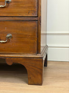 Wooden dresser with brass handles on a wooden floor.