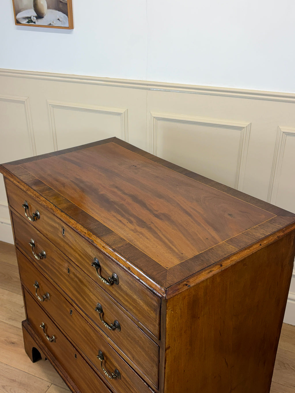 Wooden dresser with four drawers against a white paneled wall.