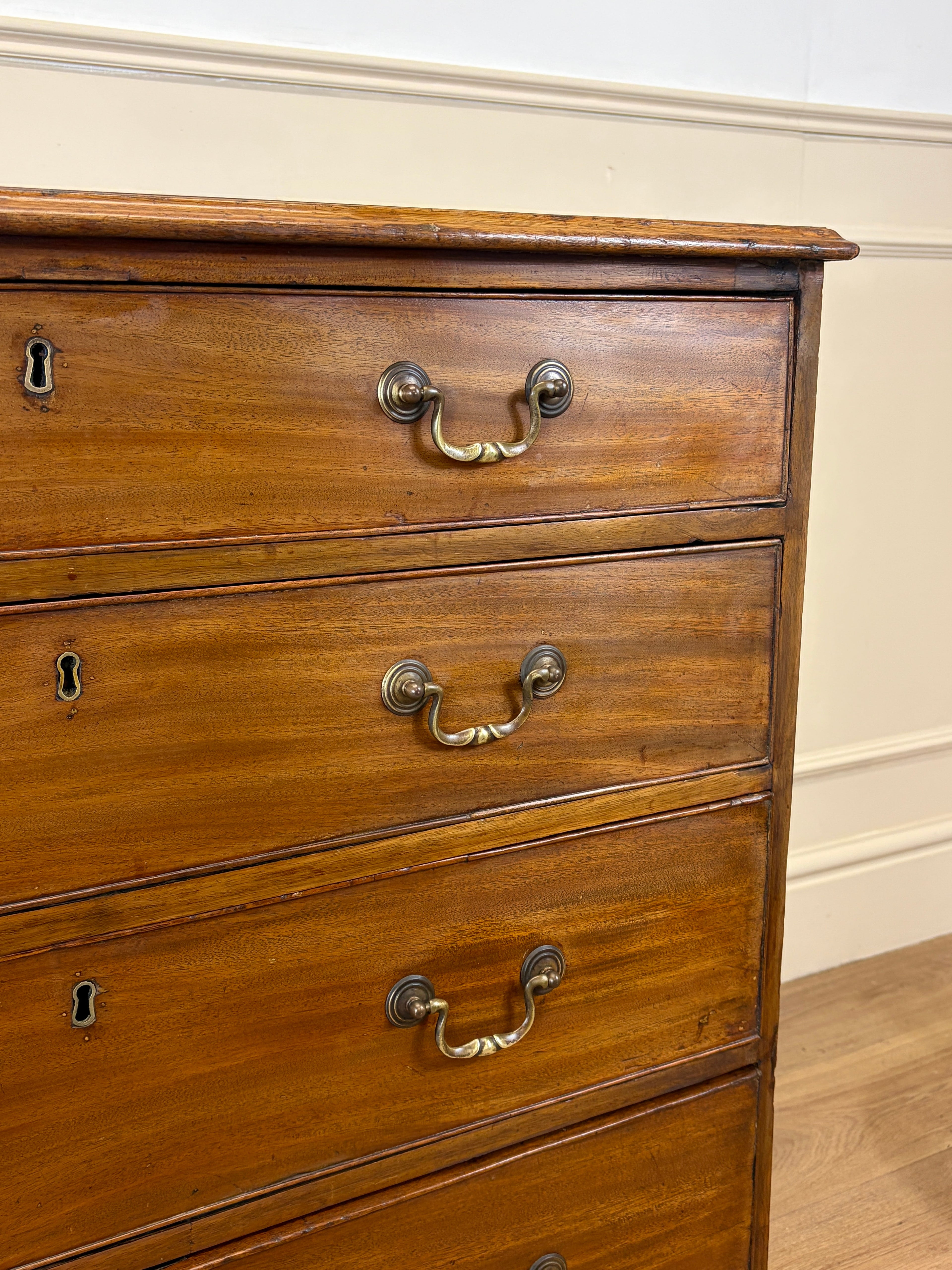 Wooden dresser with brass handles against a beige wall.