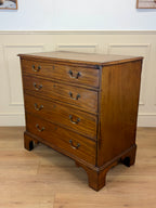 Wooden dresser with four drawers on a wooden floor against a white wall.