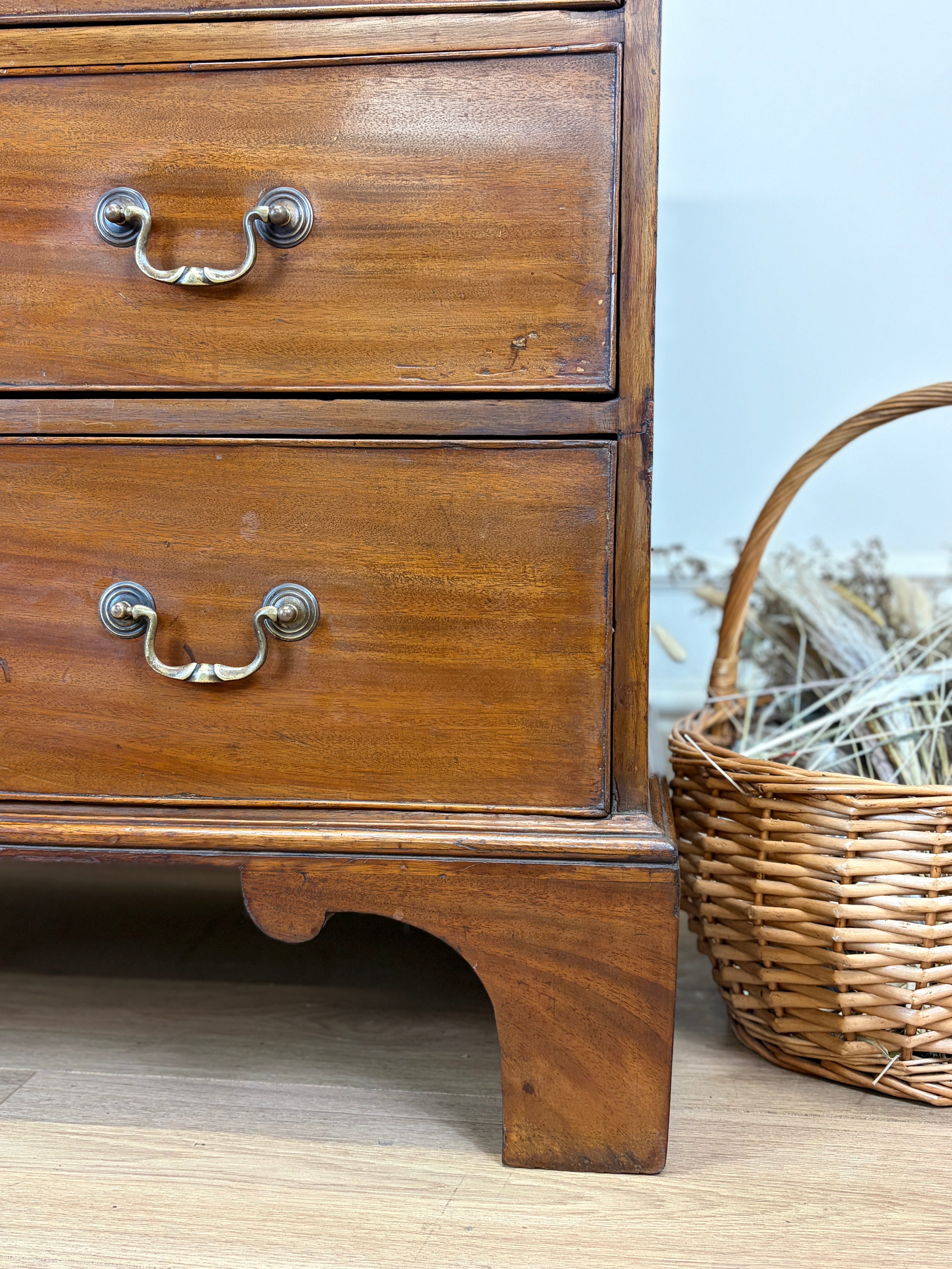 Wooden dresser with two drawers and a wicker basket on a wooden floor.