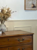 Wooden dresser with decorative vase and dried plants against a light wall.