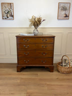 Wooden dresser with a vase of flowers on top in a room with wooden flooring and framed pictures on the wall.