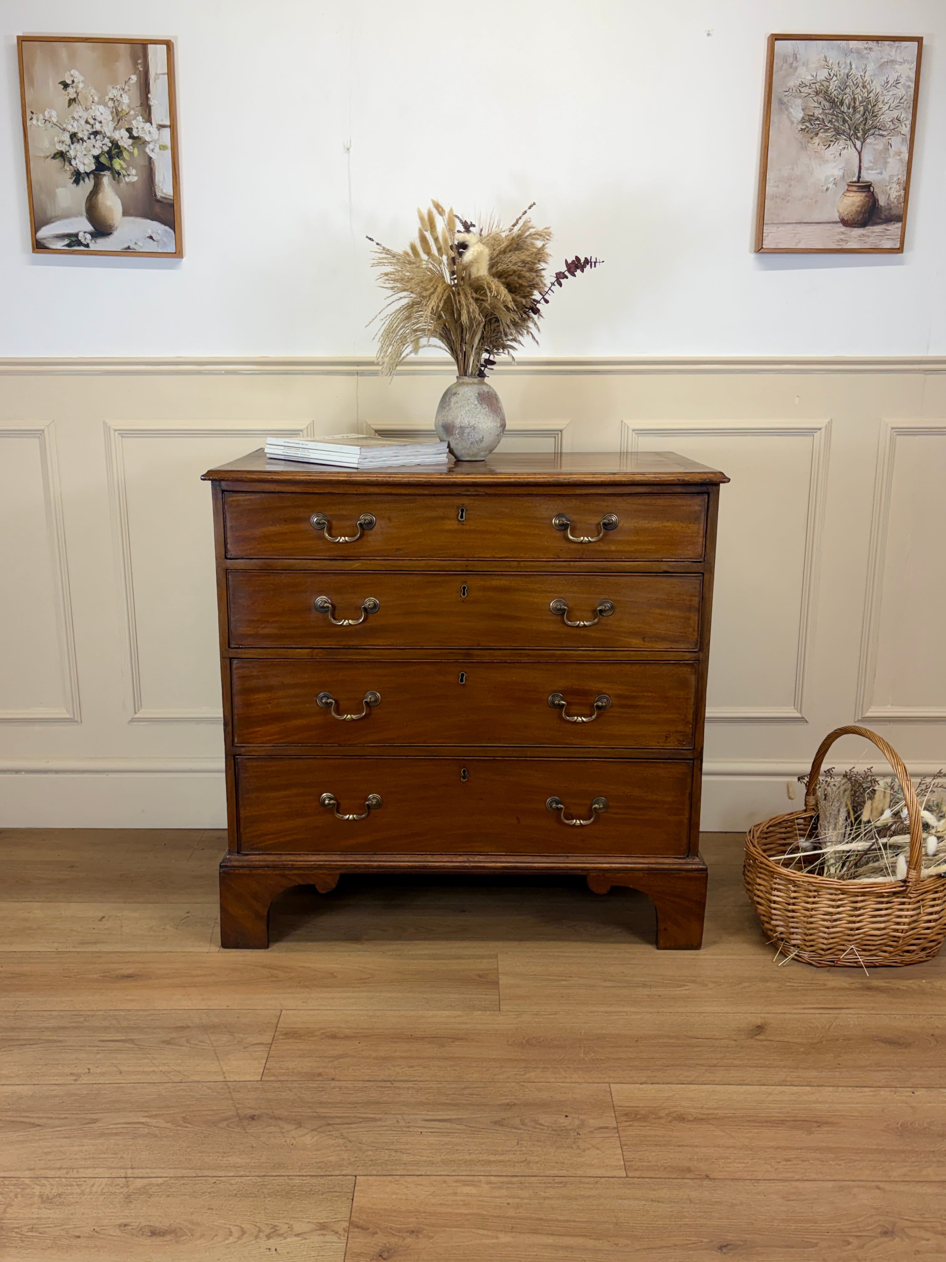 Wooden dresser with a vase of flowers on top in a room with wooden flooring and framed pictures on the wall.