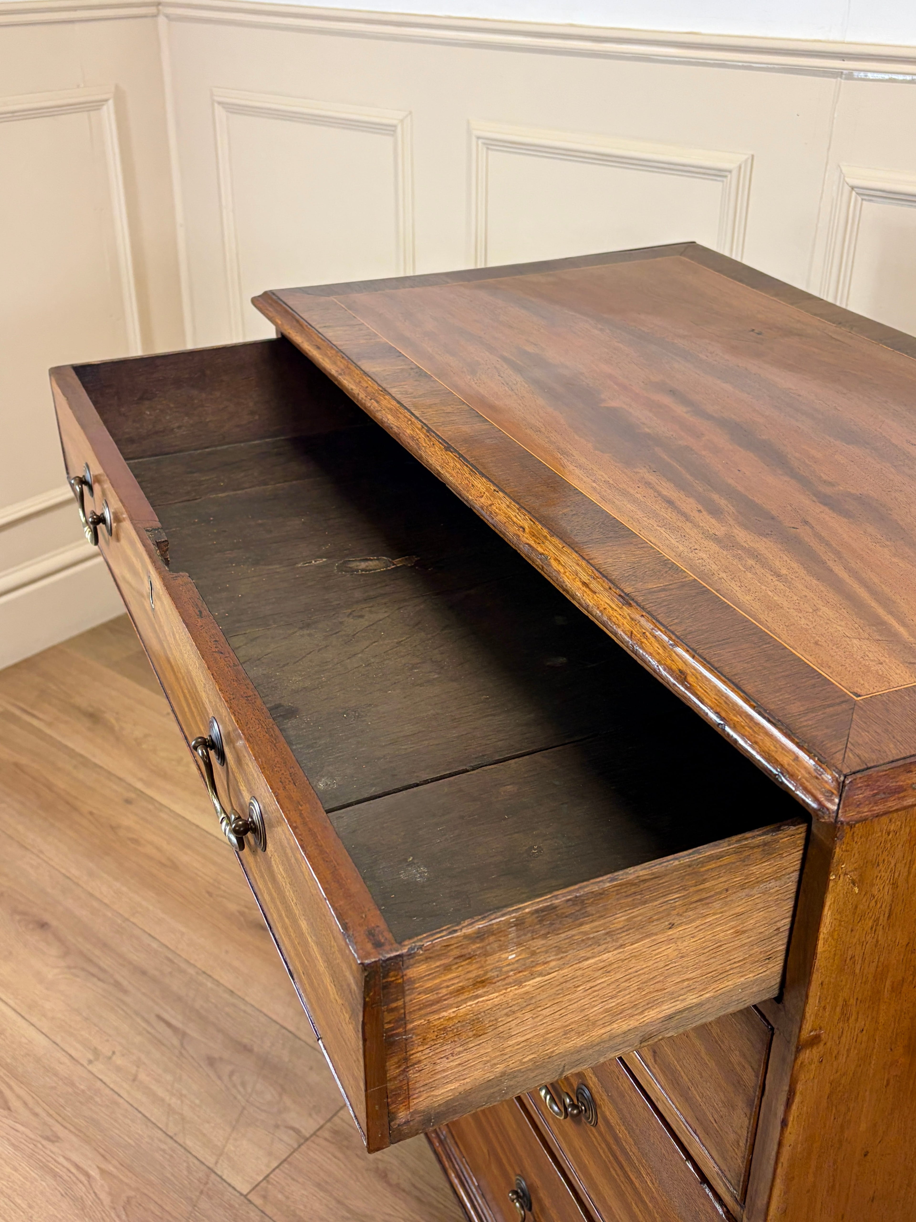 Wooden desk with an open drawer in a room with white paneled walls.