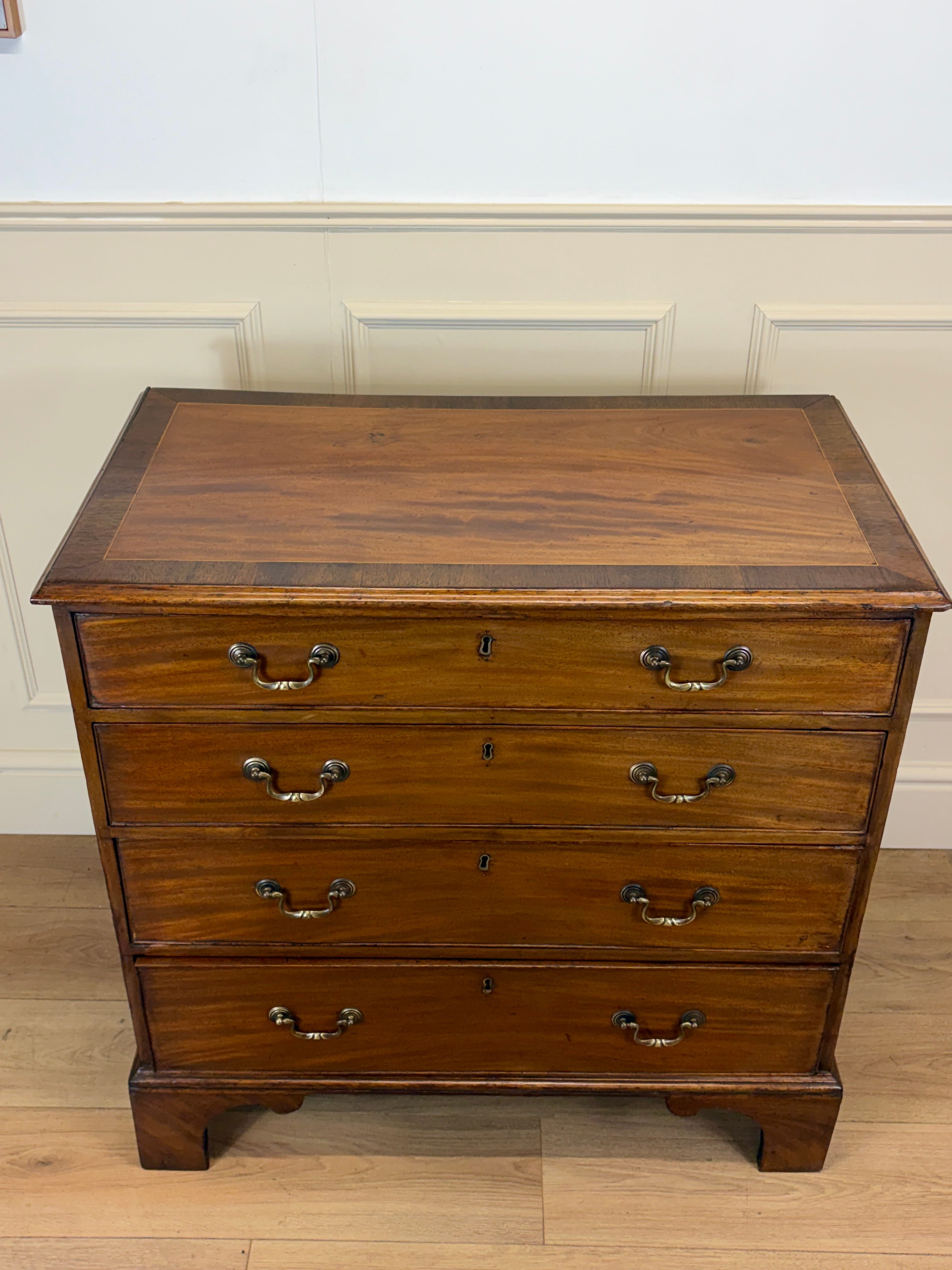 Wooden dresser with four drawers on a wooden floor against a white wall.