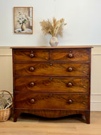 Wooden dresser with decorative items on a light wood floor and white wall.