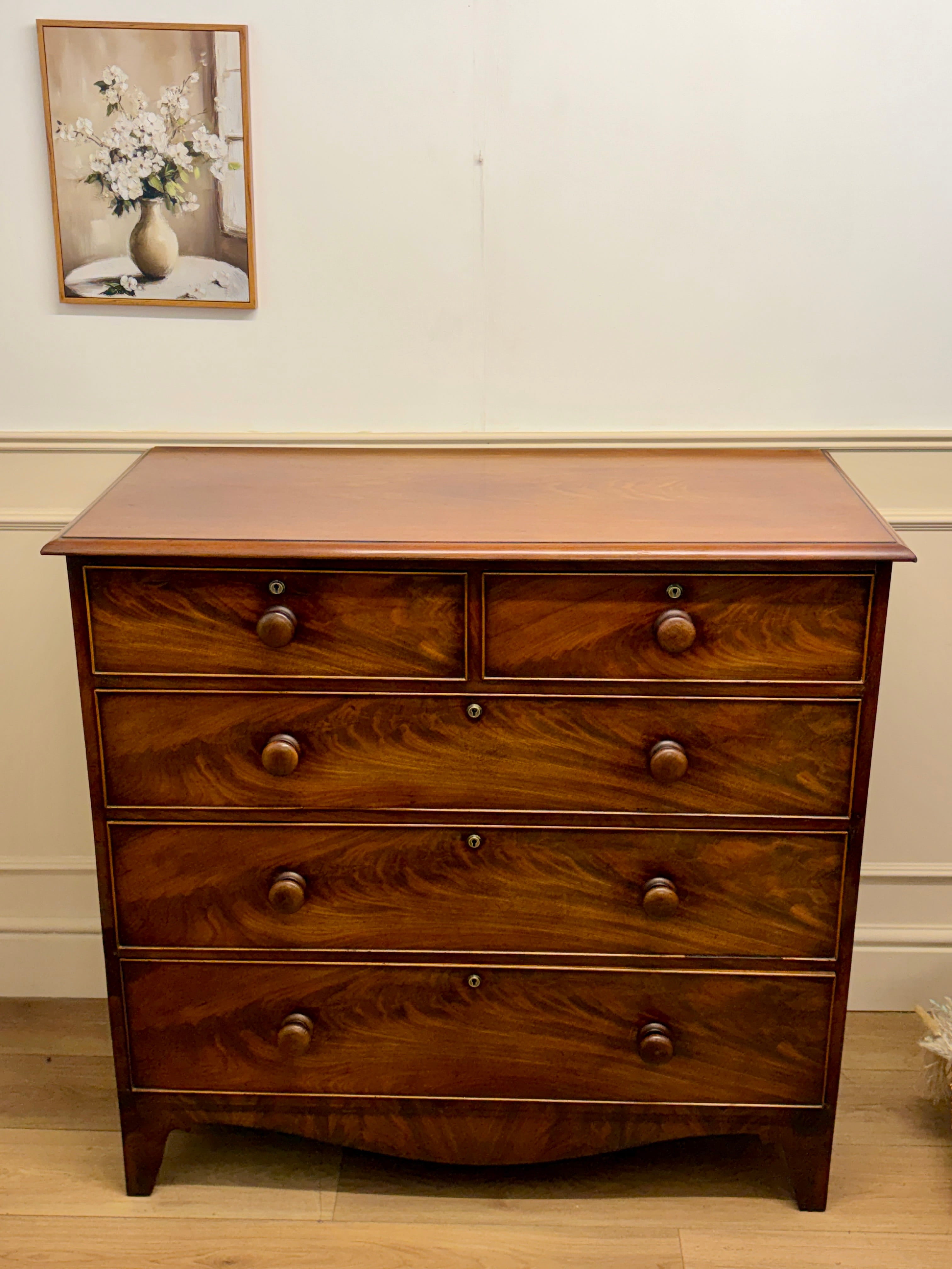 Wooden dresser with four drawers in a room with a framed picture on the wall.