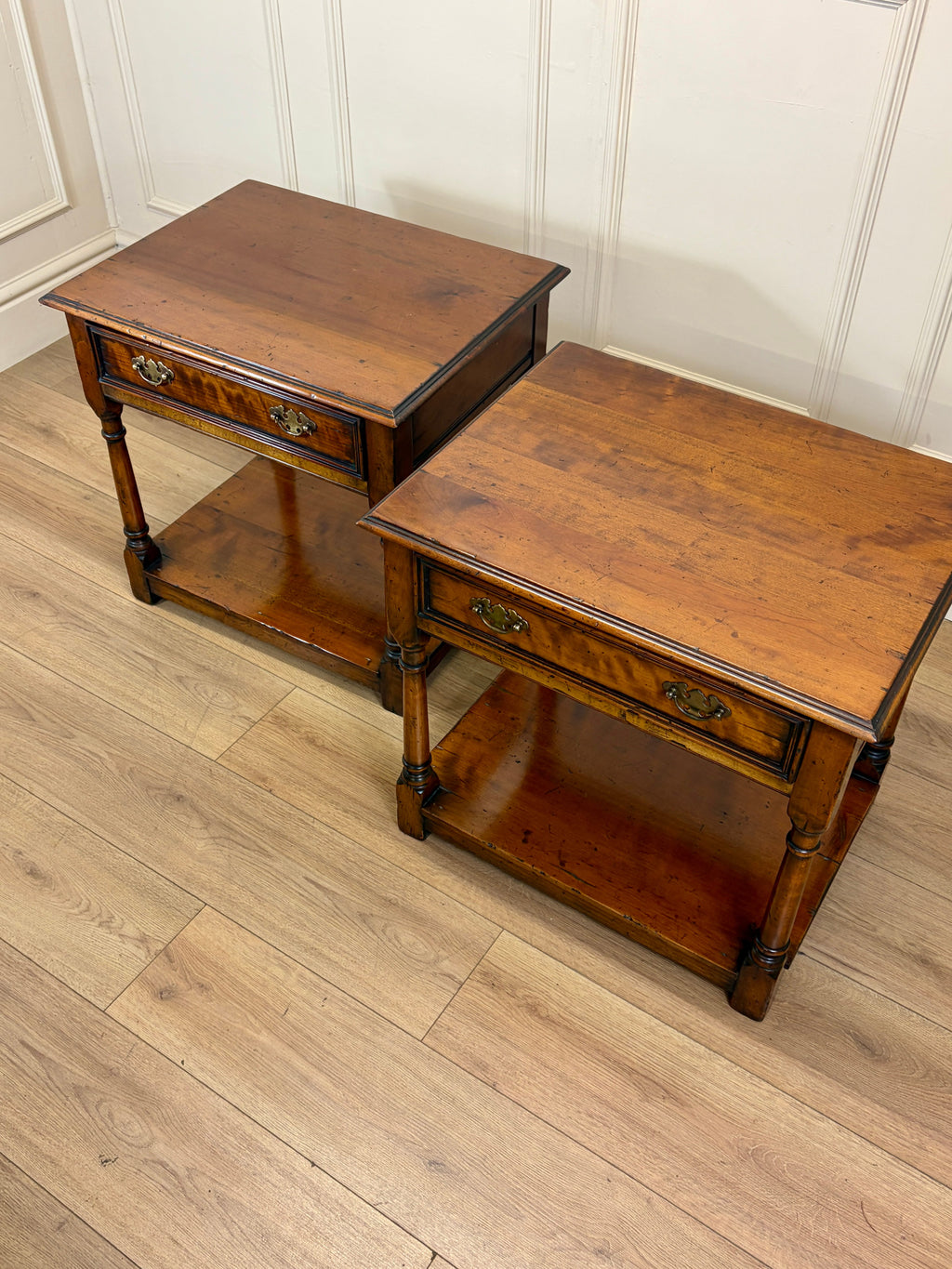 Two wooden side tables on a wooden floor with a white paneled wall in the background.