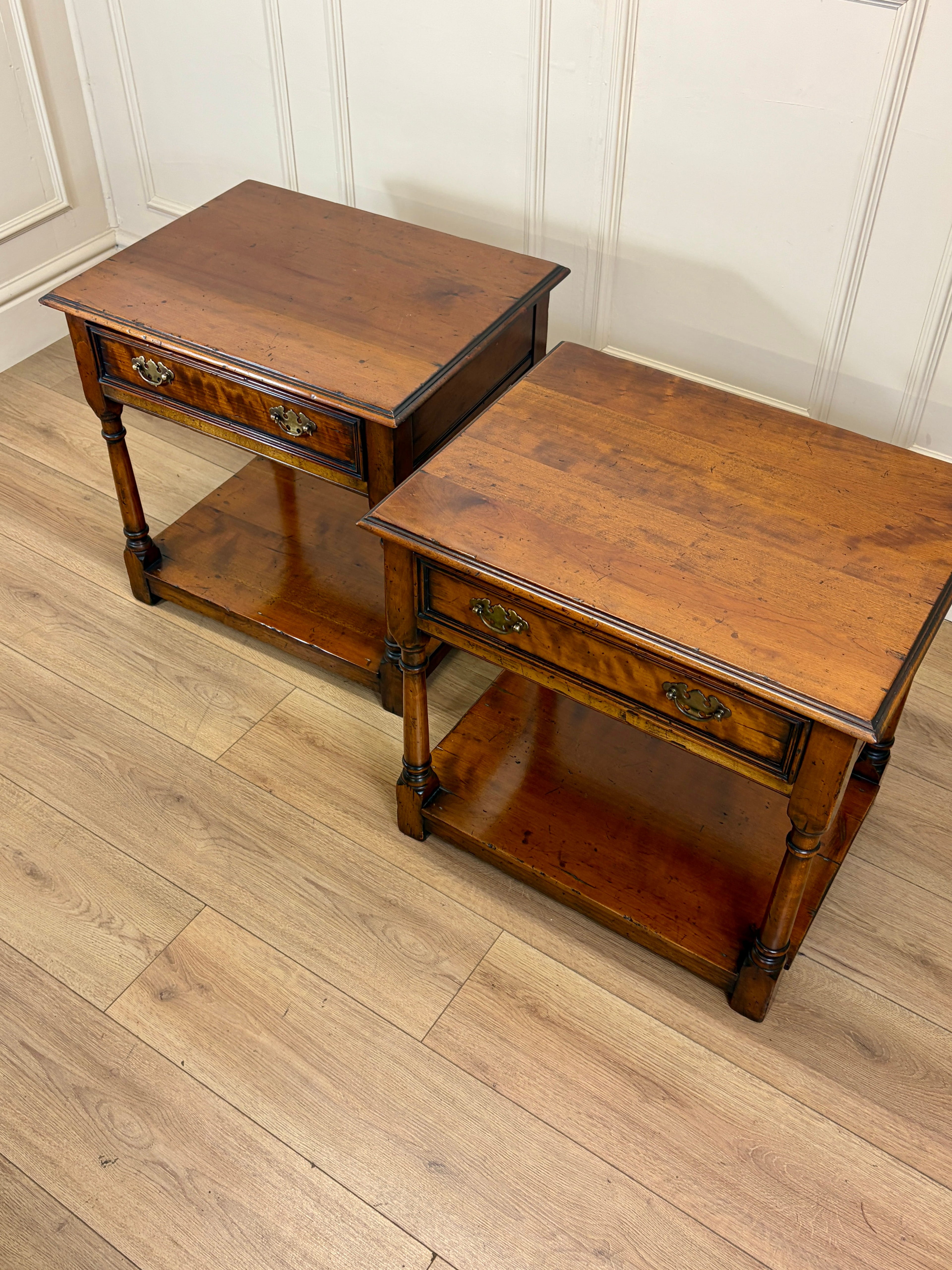 Two wooden side tables on a wooden floor with a white paneled wall in the background.