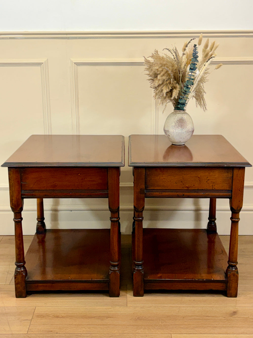 Two wooden side tables with a vase of dried flowers on a beige wall background