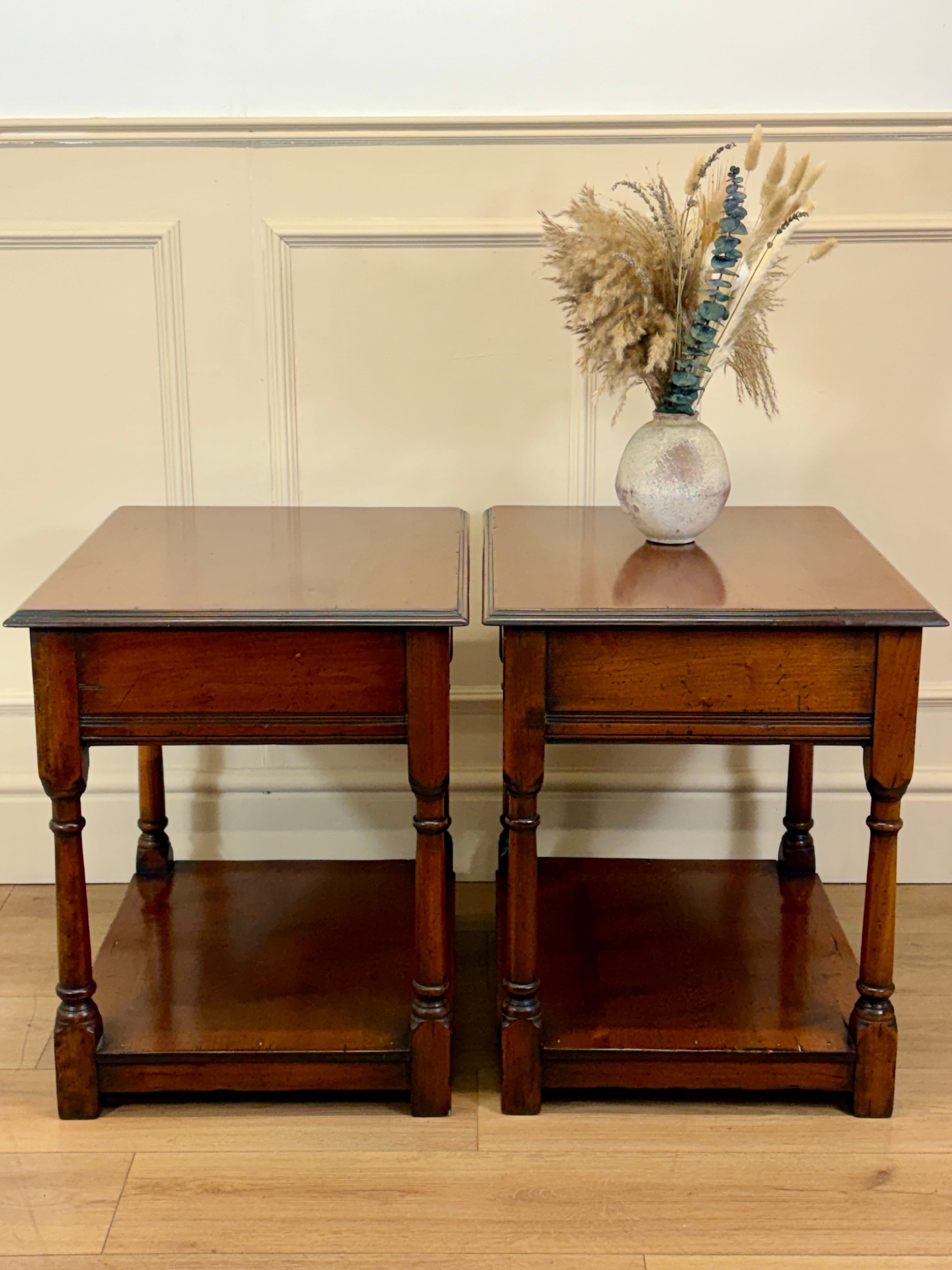 Two wooden side tables with a vase of dried flowers on a beige wall background