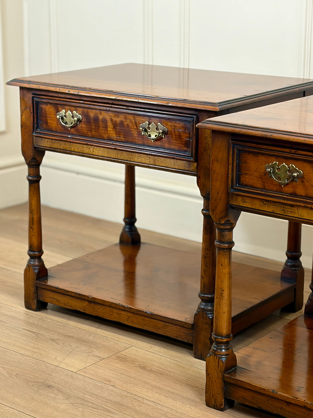 Pair of wooden side tables with drawers on a wooden floor.