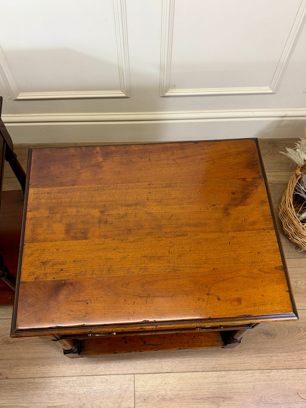Wooden side table with a worn surface in a room with white walls and wooden flooring.
