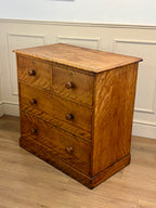 Wooden dresser with four drawers on a wooden floor against a white paneled wall.