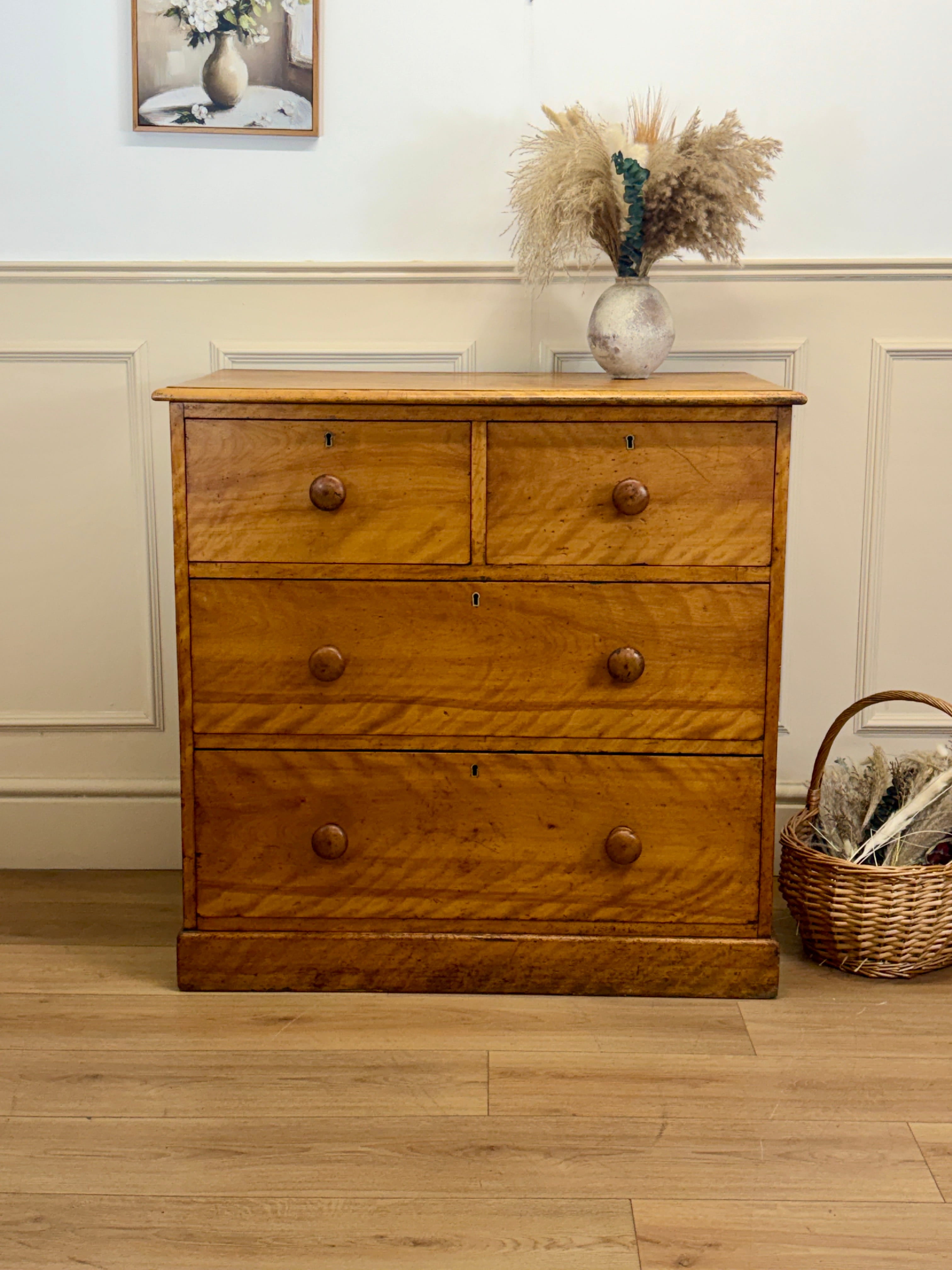 Wooden dresser with four drawers on a wooden floor, with a basket and decorative items in the background.