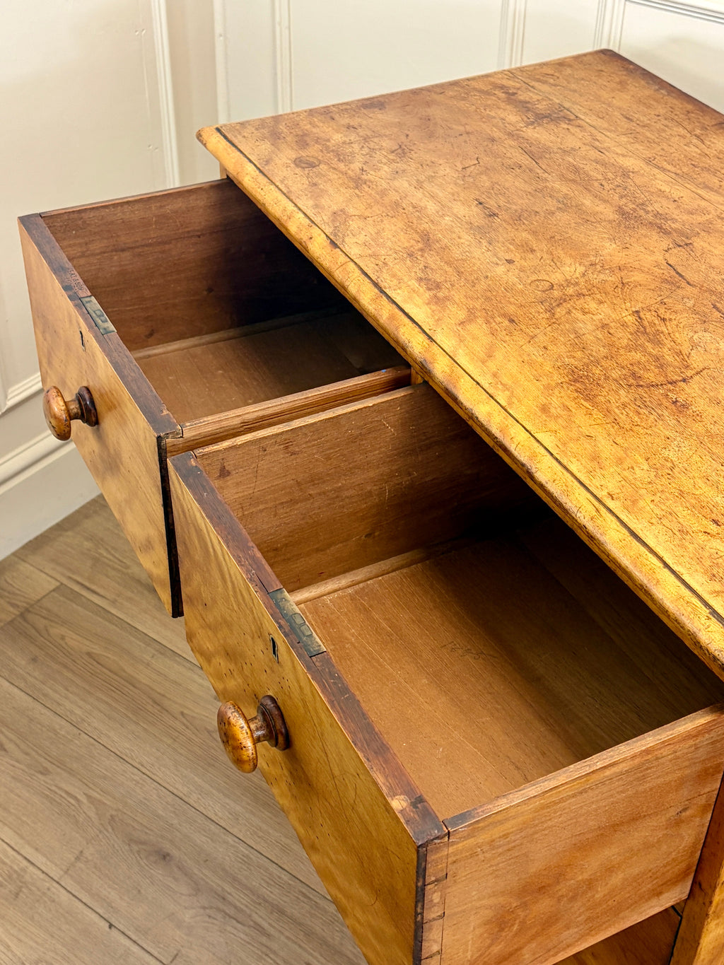 Wooden desk with open drawers against a white wall.