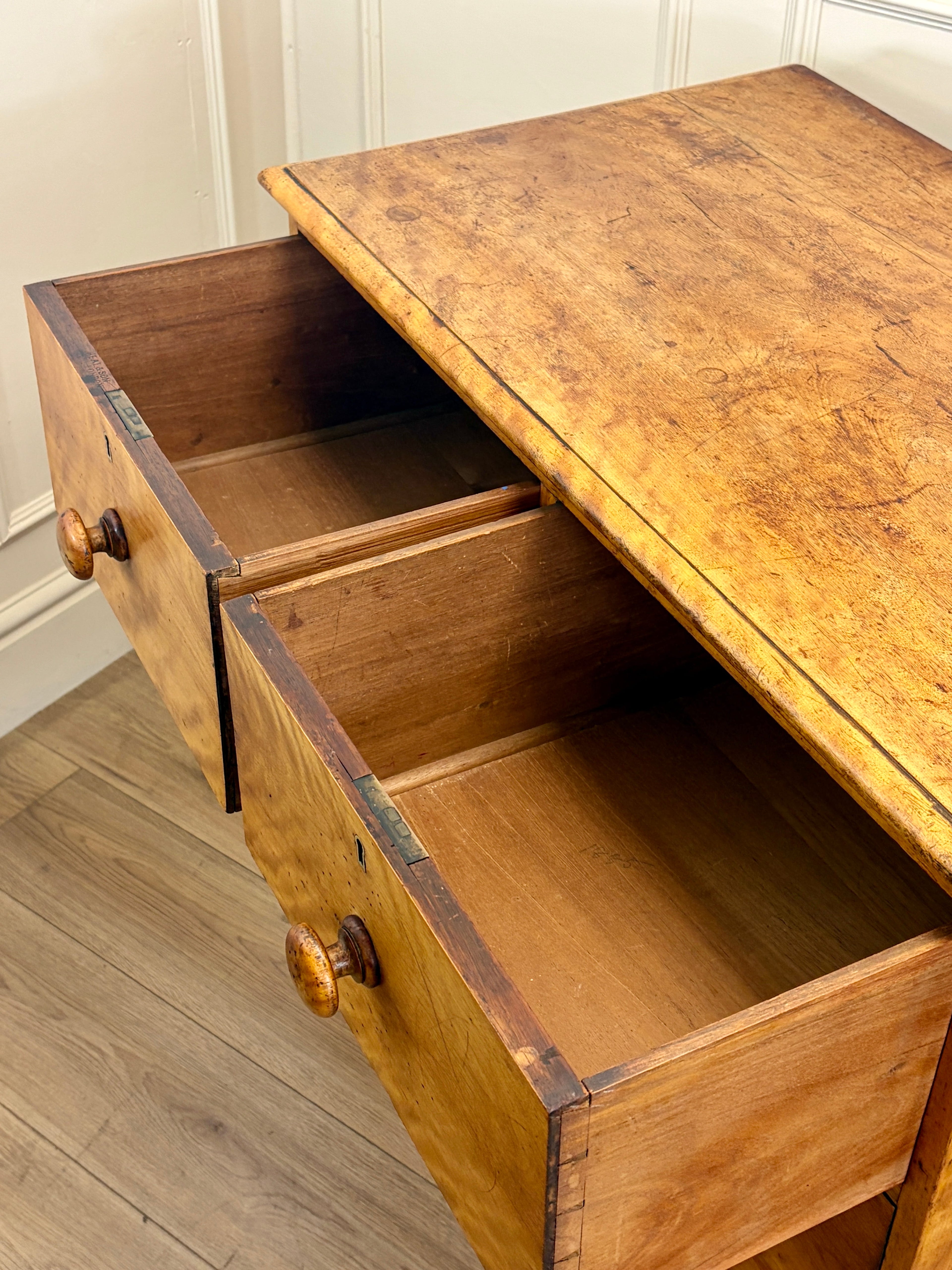 Wooden desk with open drawers against a white wall.