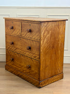 Wooden dresser with four drawers on a wooden floor against a white wall.