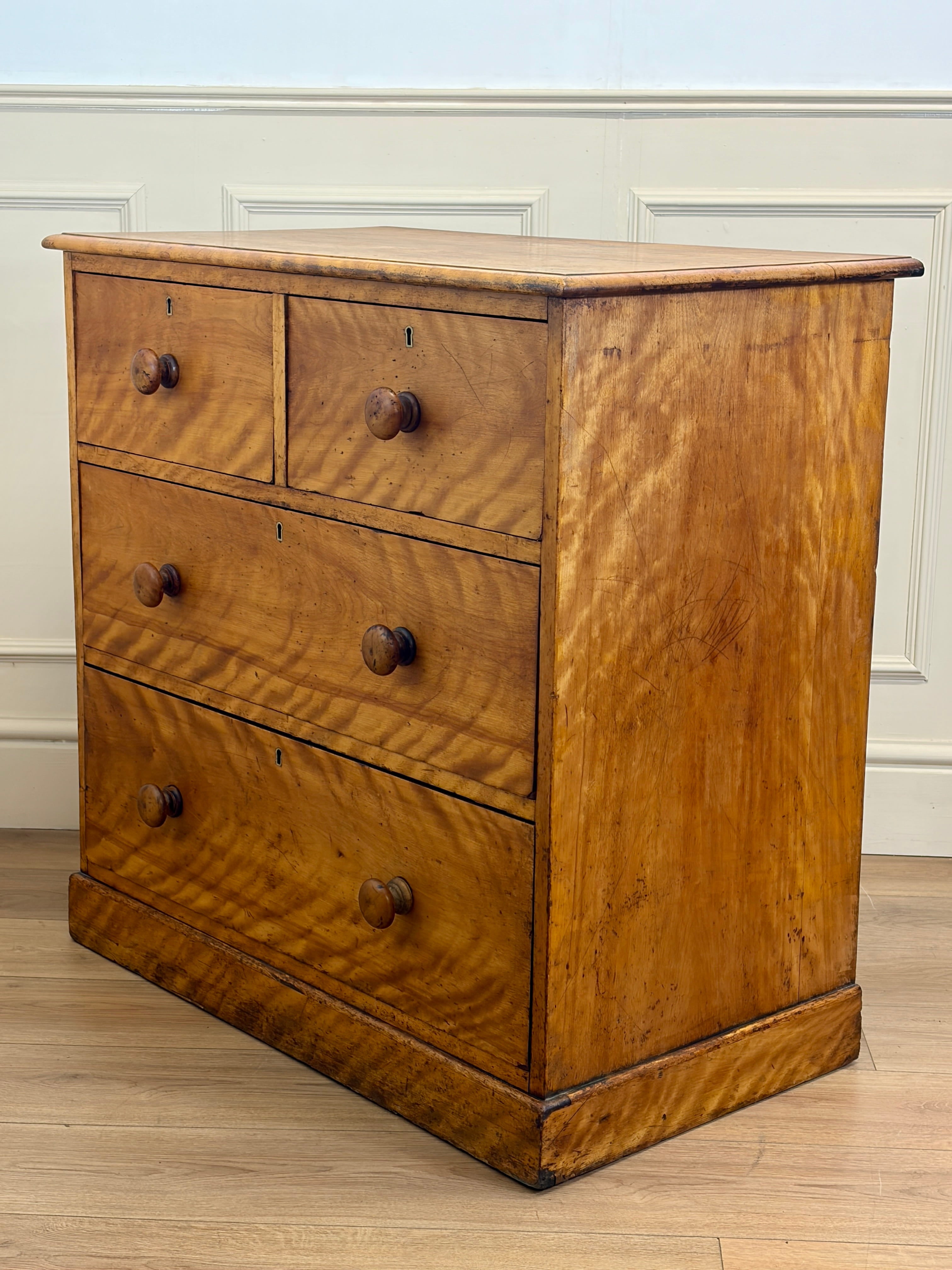 Wooden dresser with four drawers on a wooden floor against a white wall.