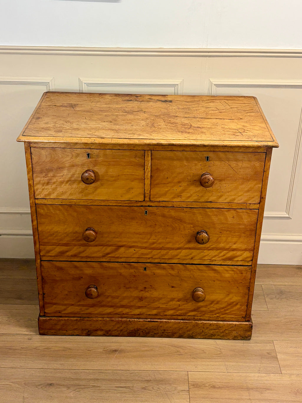 Wooden dresser with four drawers on a wooden floor against a white wall.